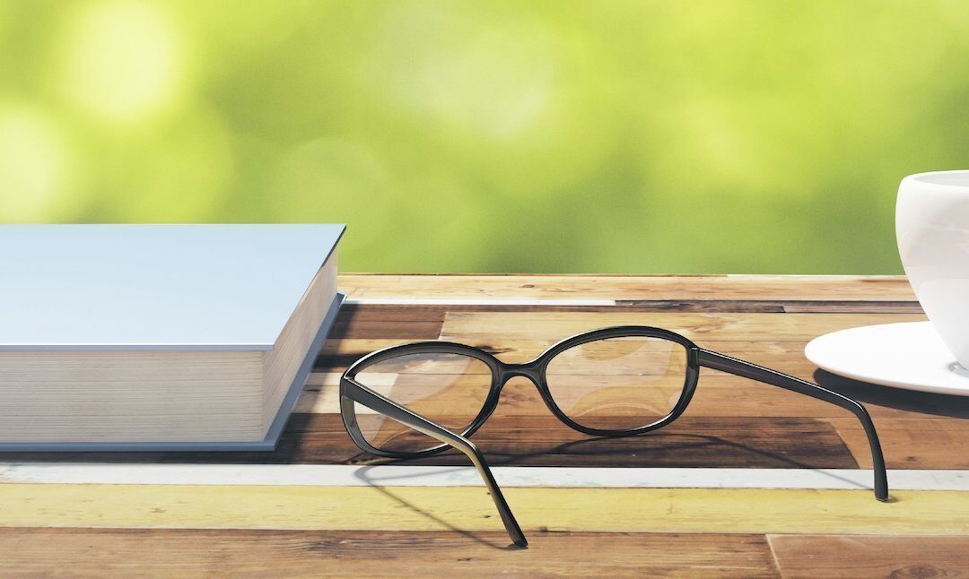 Book, cup of coffee and eyeglasses on a vintage wooden table in nature