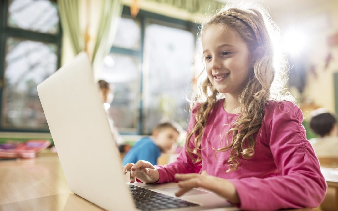 Smiling elementary student using laptop in the classroom.