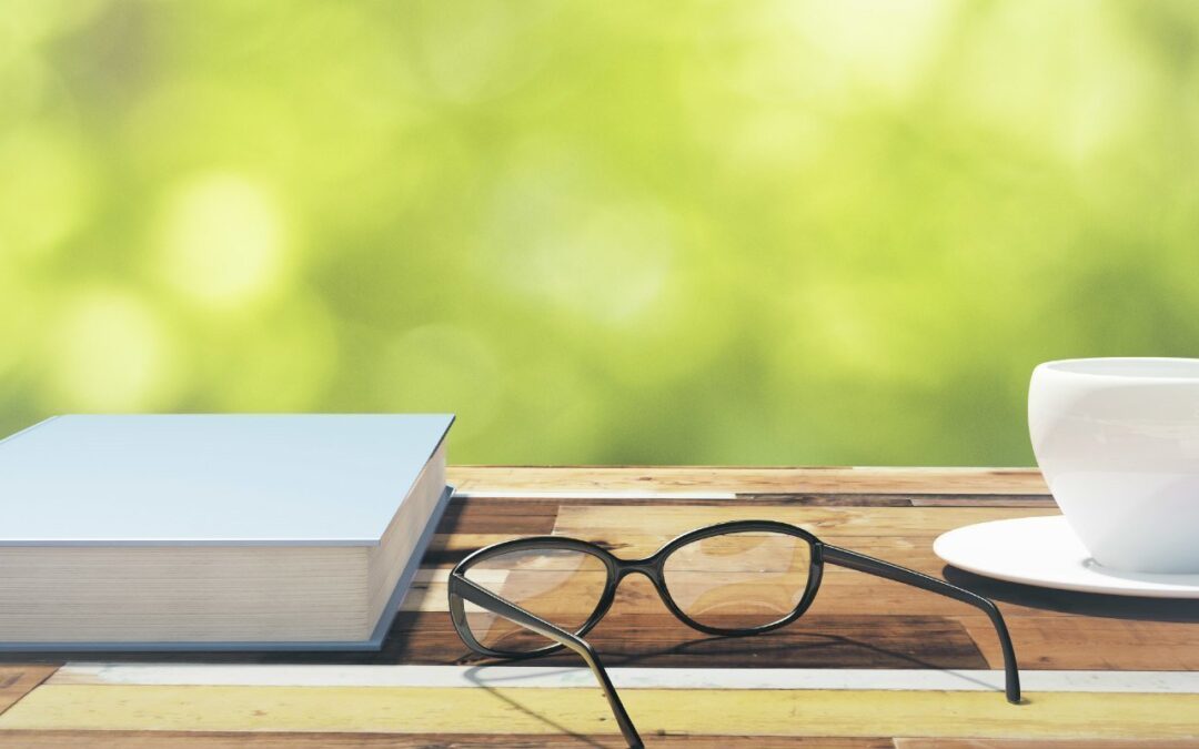 Book, cup of coffee and eyeglasses on a vintage wooden table in nature